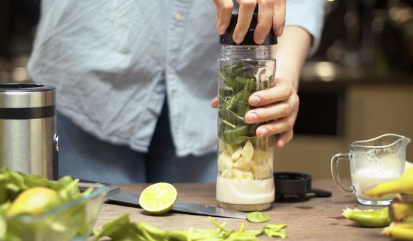 Female hands closing the blender glass with smoothie ingredients. Cooking smoothies in the kitchen. Healthy lifestyle and eating concept