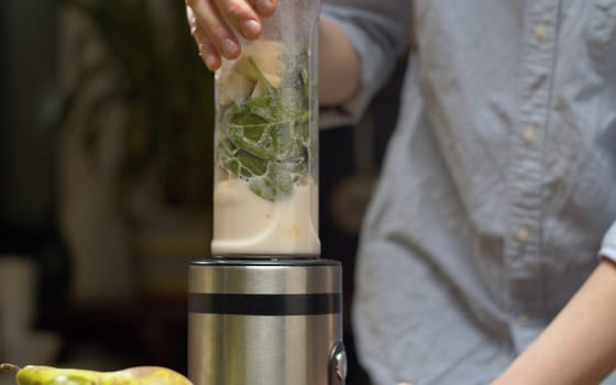 Cooking smoothies in the kitchen. Green banana spinach smoothie blended in blender. Cooking smoothies in the kitchen. Healthy lifestyle and eating concept