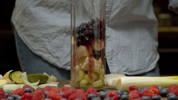 Close up pouring water in blender glass with banana, blackberry and celery slices. Fresh healthy food