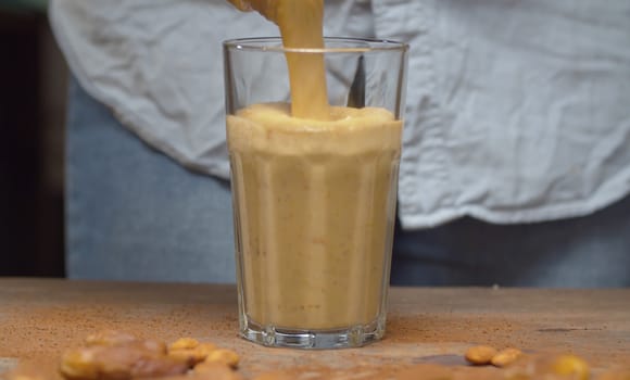 Banana almond smoothie pouring it into a glass. Cooking smoothies in the kitchen. Healthy lifestyle and eating concept