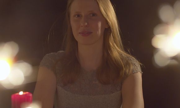 Close up portrait of beautiful caucasian woman celebrating indoors. Burning candle and blurred sparklers in the foreground.