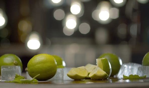 Close up sliced limes on the table over background of blurry light bulbs. Cooking of refreshing drinks.