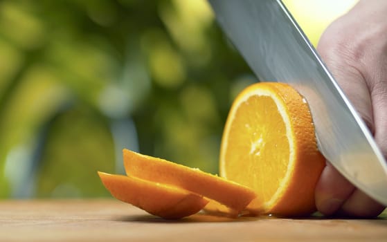 Close up male hand slicing an orange on green natural background. Juicy fruits. Healthy lifestyle and eating concept