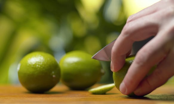 Close up male hand cutting a lime on green natural background. Making drinks. Healthy lifestyle and eating concept.