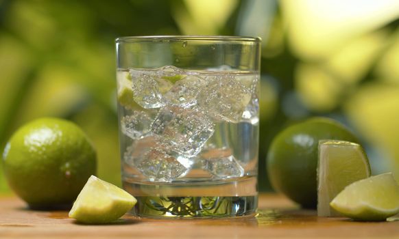 Close up tonic, soda sparkling water in a glass with ice and piece of lime on a green background. Refreshing mineral water, preparing of drinks, cocktails. Cold lemonade drink