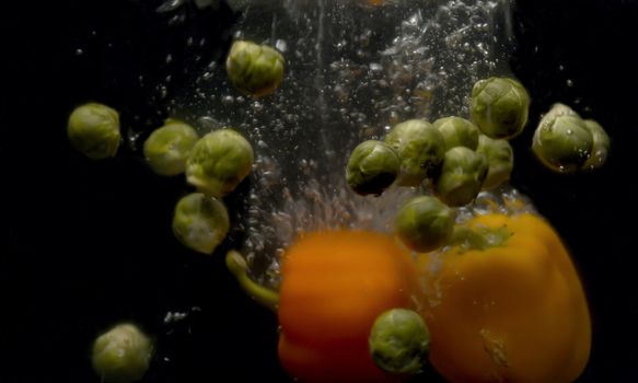 Close up brussels sprouts and paprika falling into the water with a splash and bubbles on black background