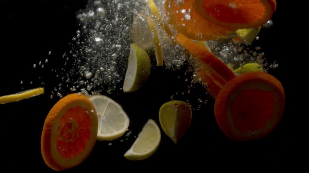 Close up sliced fresh lemons and oranges falling into the water on black background