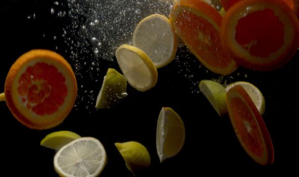 Close up sliced fresh lemons and oranges falling into the water on black background