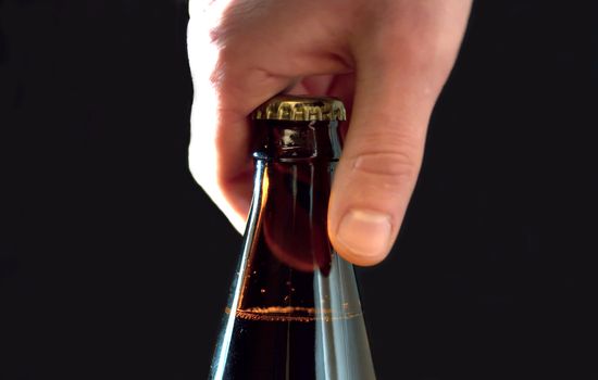 Close up man's hand opening a bottle of beer, side view, black background.