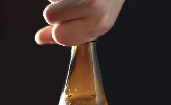 Close up man's hand opening the bottle of beer on black background. Foam and bubbles begin to rise in the bottle