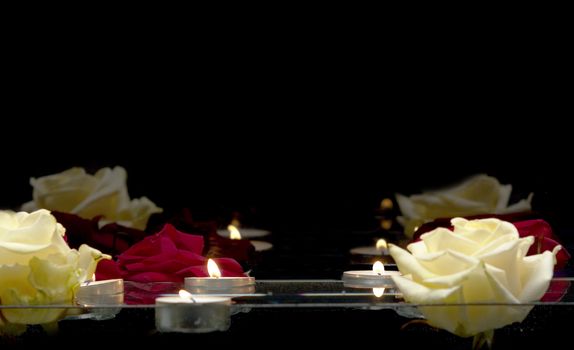 Close up shot of burning candles and roses floating on the water on a black background