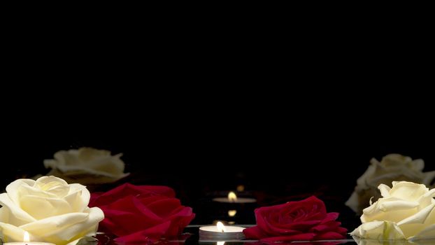 Close up shot of burning candles and roses floating on the water on a black background