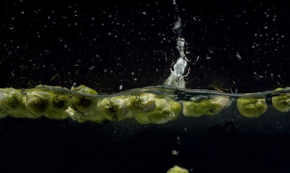 Close up brussels sprouts falling into the water with a splash and bubbles on black background