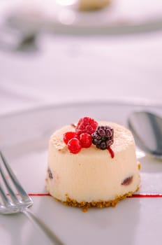 Vanilla and Red Fruits Dessert Cake served with Cookie Base served on a white plate with spoon and fork