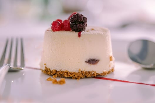 Vanilla and Red Fruits Dessert Cake served with Cookie Base served on a white plate with spoon and fork