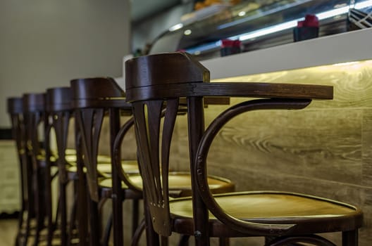 Classic dark wood stools arranged in a row on a bar with a wood texture and lower warm lighting