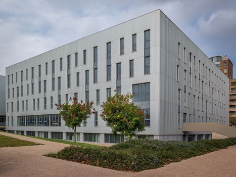 Perspective of the exterior of the Valencia conservatory, showing the trees and concrete paths; with the soft morning light of a cloudy sky. Accentuating the textures of the facade & windows.