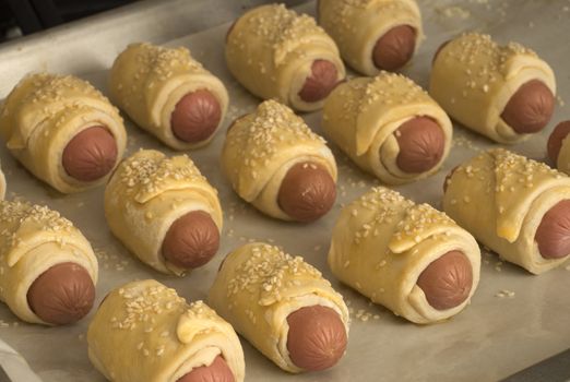 Raw sausages in the dough with sesame on a baking sheet are ready for baking. Close up. Cooking food at home.