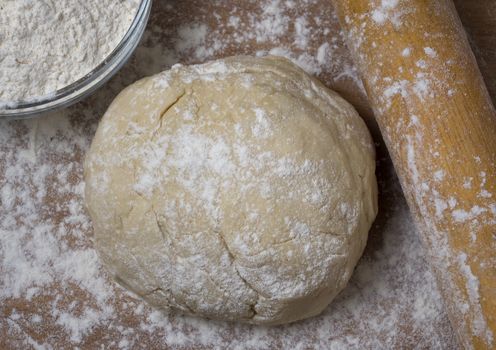 Fresh raw dough for pizza or bread baking on wooden cutting board.