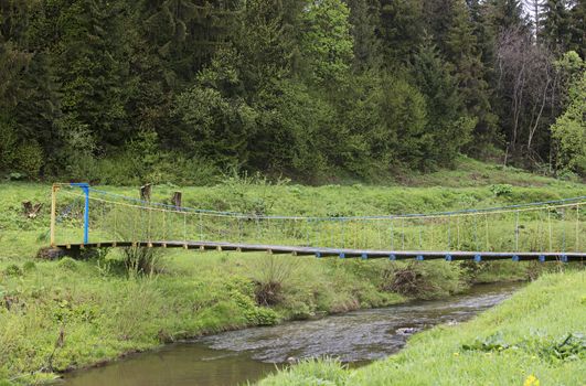 Suspension bridge over the mountain river among the bright green forest, Carpathians Ukraine