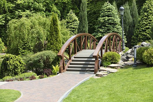 A small wooden bridge over the creek and paved sidewalk beautifully complements the general view of landscape design