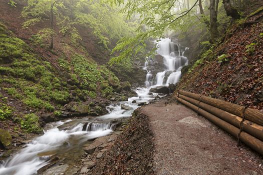 A well-groomed path to the waterfall along the fast mountain river between the hills of the Carpathian Mountains.