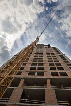 The new house that is being built, and the tower crane, rest against the blue sky with light clouds and touch the flying birds