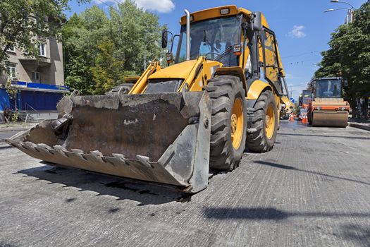 Heavy construction bulldozer and vibrating roller during the construction of a road on a city street at noon