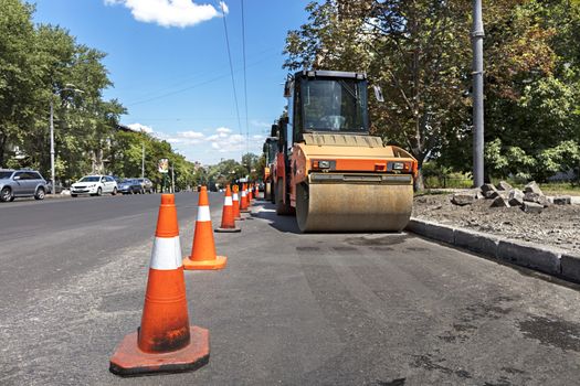 Orange road cones protect the working area for heavy vibrating compactors on a city street