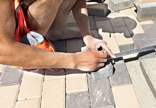 The worker measures a bar of sidewalk tiles for the final laying on the terrace