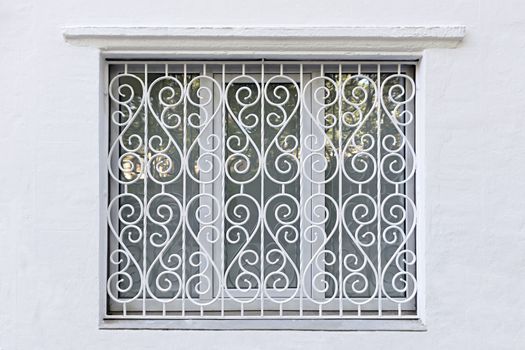 Window on the white wall. Figured frame of the window hole. Iron wrought-iron lattice curly painted white