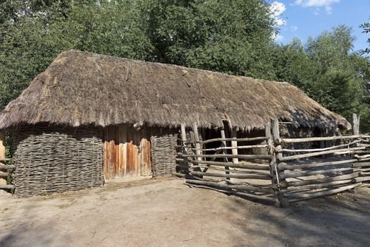 The old traditional woven Ukrainian rural barn with a thatched roof and a wooden fence around it in the courtyard