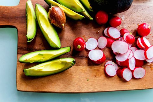 Sliced avocado and radish on a wooden chopping board