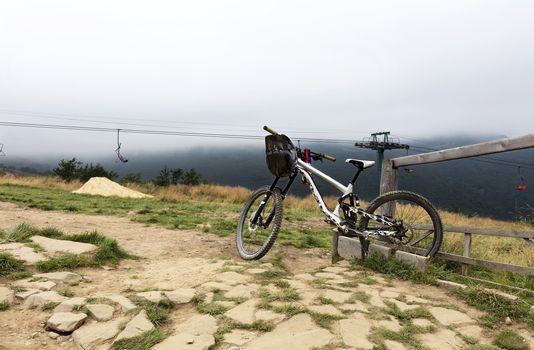Carpathians. The cyclist left a mountain bike for a respite. The lift is in a thick fog in the background of a mountain landscape.