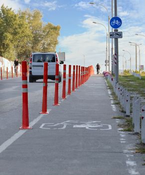 bike path in the park with busy traffic fenced with red road columns against the blue sky and the setting sun