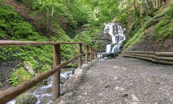 A well-groomed path to the waterfall along the fast mountain river between the hills of the Carpathian Mountains.