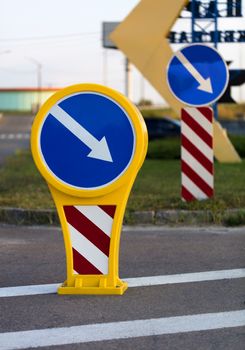 Round bright yellow-blue road sign detour on the right with white-red diagonal warning stripes standing on the road marking