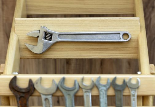 Old adjustable wrench lies on the step of a wooden ladder against the background of old wrenches
