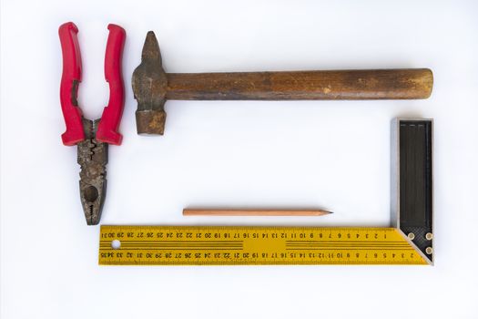 Old tools are a hammer with a wooden handle, pliers, square and pencil. Objects are isolated on a light background closeup
