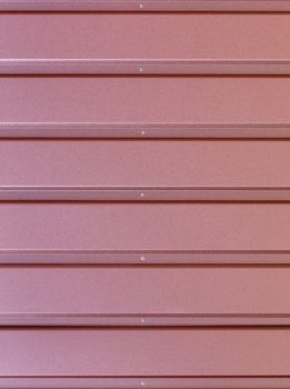 Reddish-brown metal fence made of corrugated steel sheet with gorizontal guides and metal rivets in the middle. Corrugated reddish-brown iron sheet background close up.