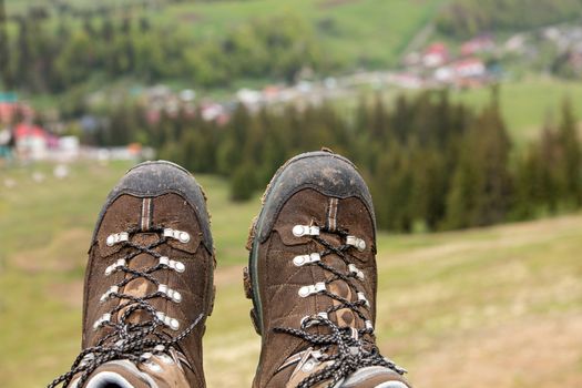 Mountain tracking boots close-up after a long trek through the mountains on a blurred green background of the valley of the summer mountains