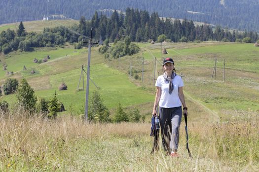 A young woman in a joyful mood travels along the slope in the Carpathians in summer against the background of a mountain landscape.