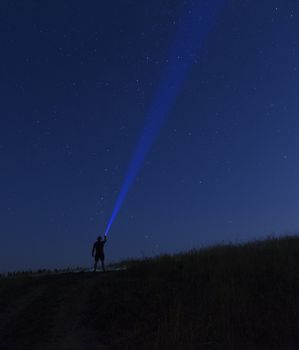 Silhouette of man on a background of stars he directs a ray of light onto a dark blue starry sky