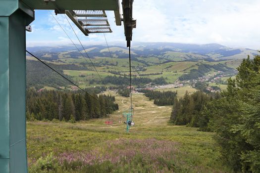 The support of the mountain lift rises above the mountains against the backdrop of the summer mountain landscape in the Carpathians