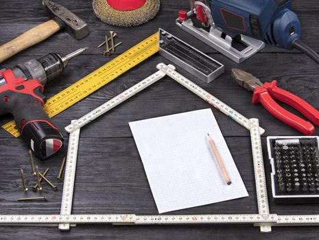 white sheet in a cell for writing with a pencil on the background of a hand-held construction tool on black old boards