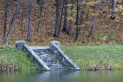 Coast of the forest pond. The smooth surface of the water reaches the old steps of the stone descent.