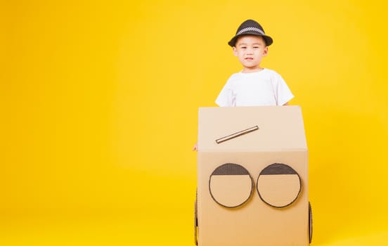 Portrait happy Asian cute little children boy smile so happy wearing white T-shirt driving car creative by cardboard, studio shot on yellow background with copy space