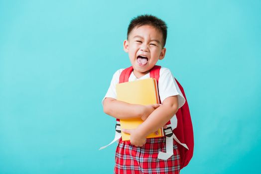 Back to school concept. Portrait Asian happy funny cute little child boy smiling and laugh hug books, studio shot isolated blue background. Kid from preschool kindergarten with school bag education