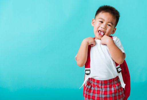Back to school concept. Portrait closeup happy Asian cute little child boy in uniform smiling, isolated blue background. The kid from preschool kindergarten with a school bag backpack