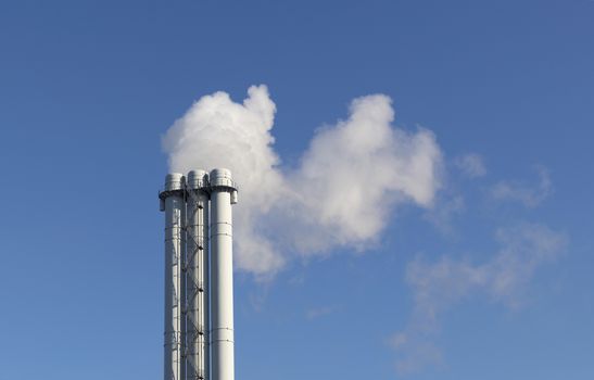 White smoke comes from a white chimney pipe on a background of blue sky. The environment. Greenhouse effect.